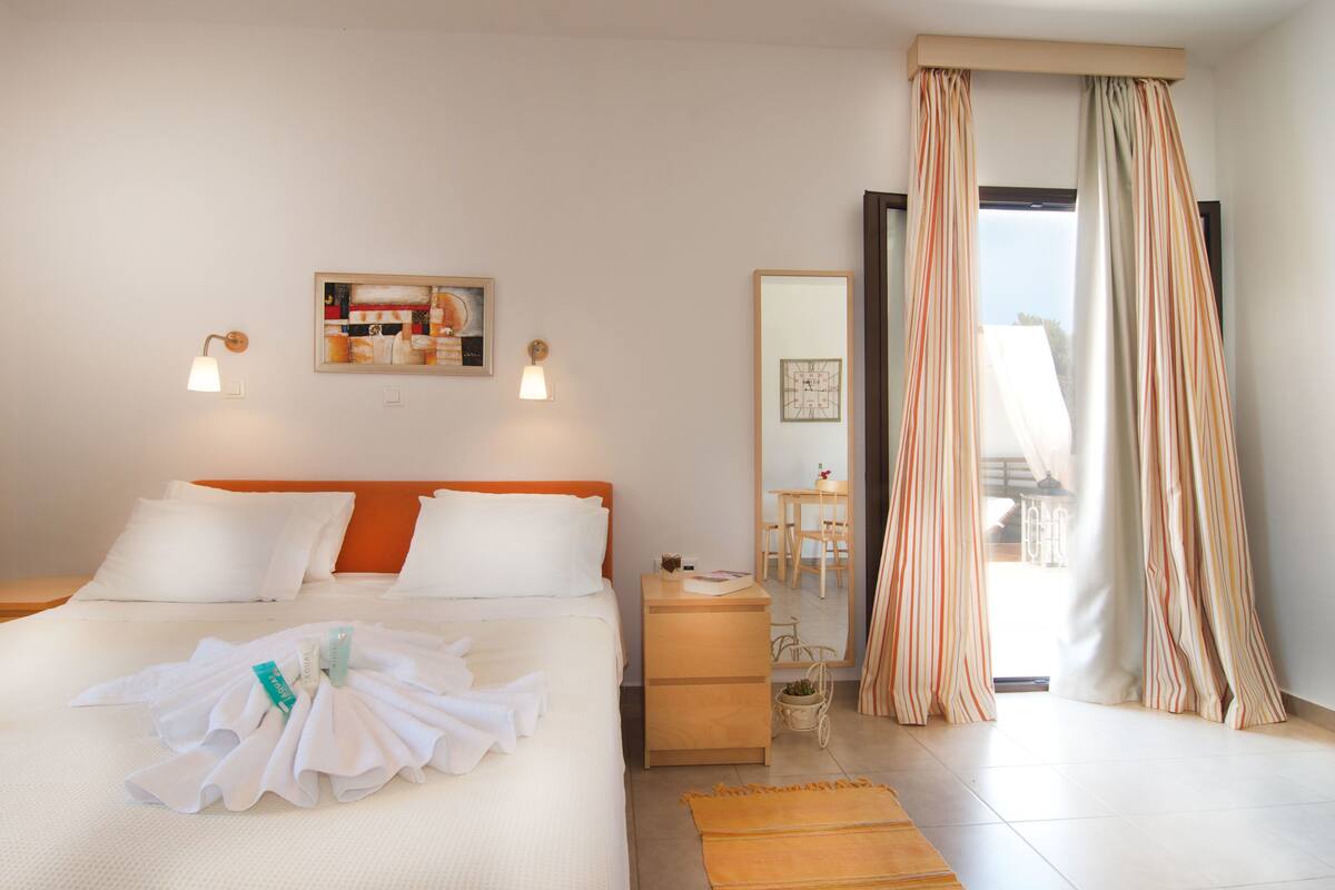 A hotel room with a bed, a bedside table, a nightstand, a mirror, and a view of the outside.