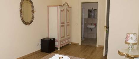 Un dormitorio con cama, armario, espejo y baño visible a través de una puerta abierta.