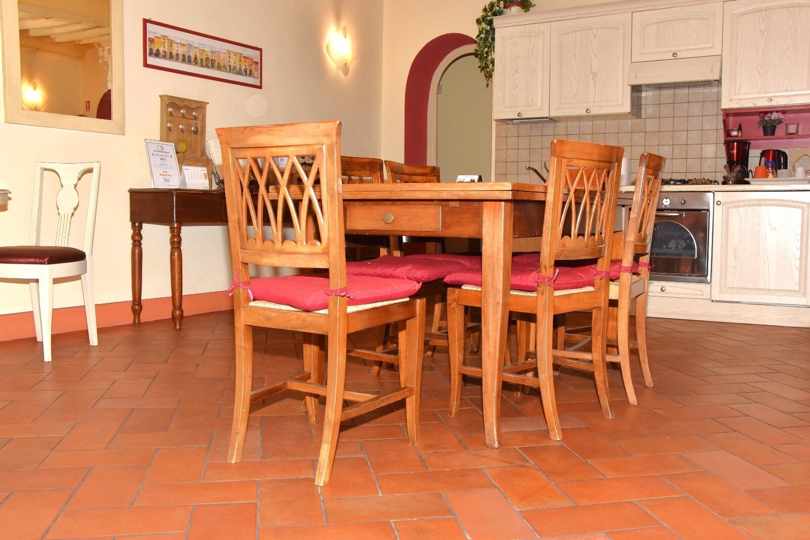 Un comedor con una mesa y sillas de madera, piso de baldosas y una cocina al fondo.