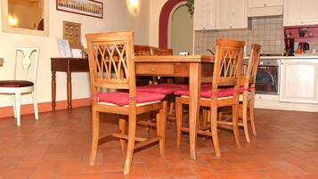 Un comedor con una mesa y sillas de madera, piso de baldosas y una cocina al fondo.