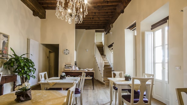 A dining area with wooden tables and chairs, a chandelier, and a staircase leading to another level. - Anfiteatro Bed and Breakfast (Lucca)