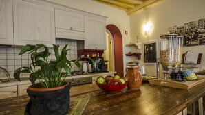 A kitchen with white cabinets, a coffee maker, a red bowl with fruits, and a coffee grinder. - Anfiteatro Bed and Breakfast (Lucca)