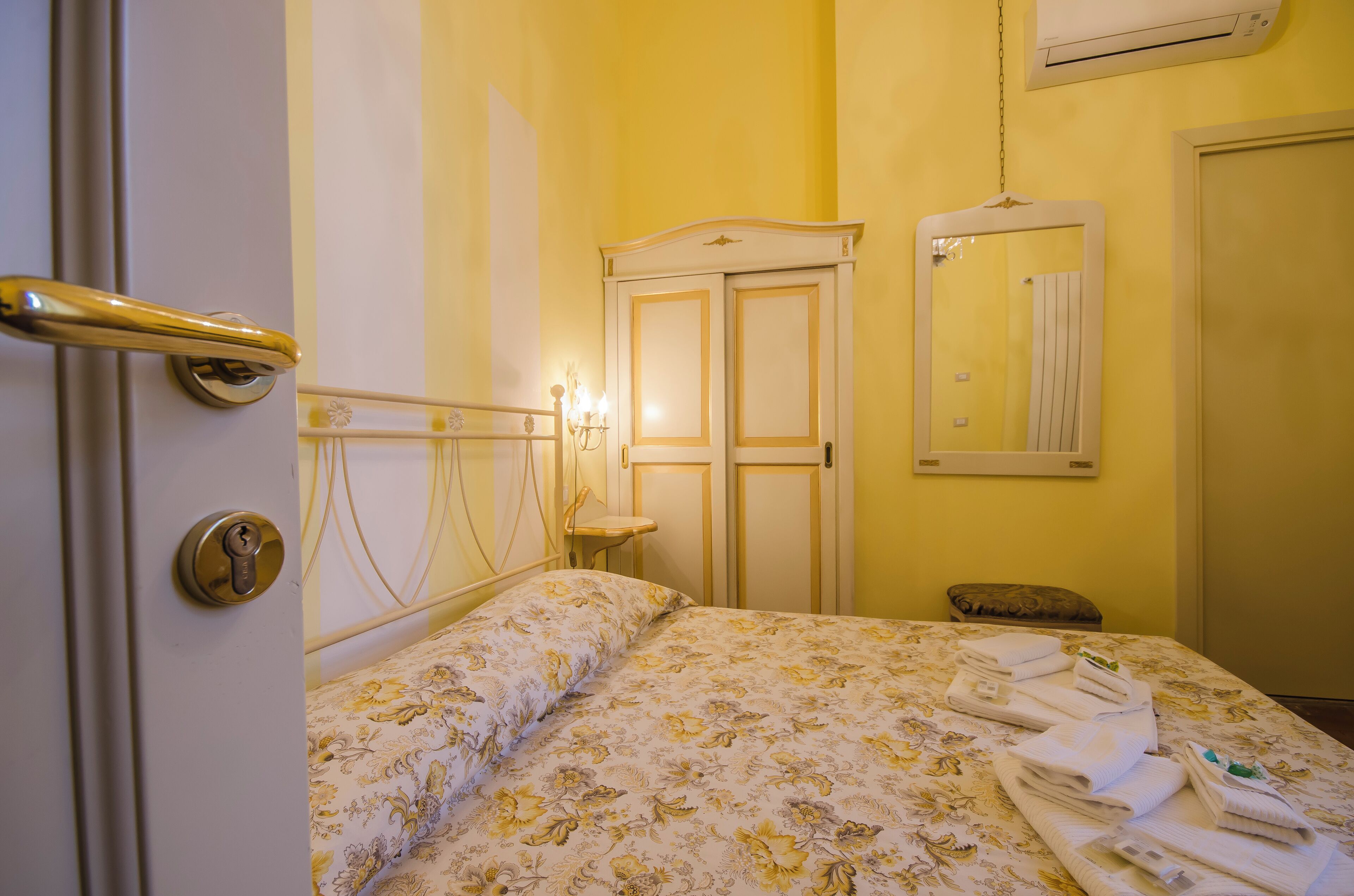 A hotel room with a bed, a bedside table, a mirror, and a door with a handle.