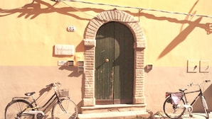 A building with a large arched door, two bicycles parked in front, and a sign indicating the name 'Anfiteatro'. - Anfiteatro Bed and Breakfast (Lucca)