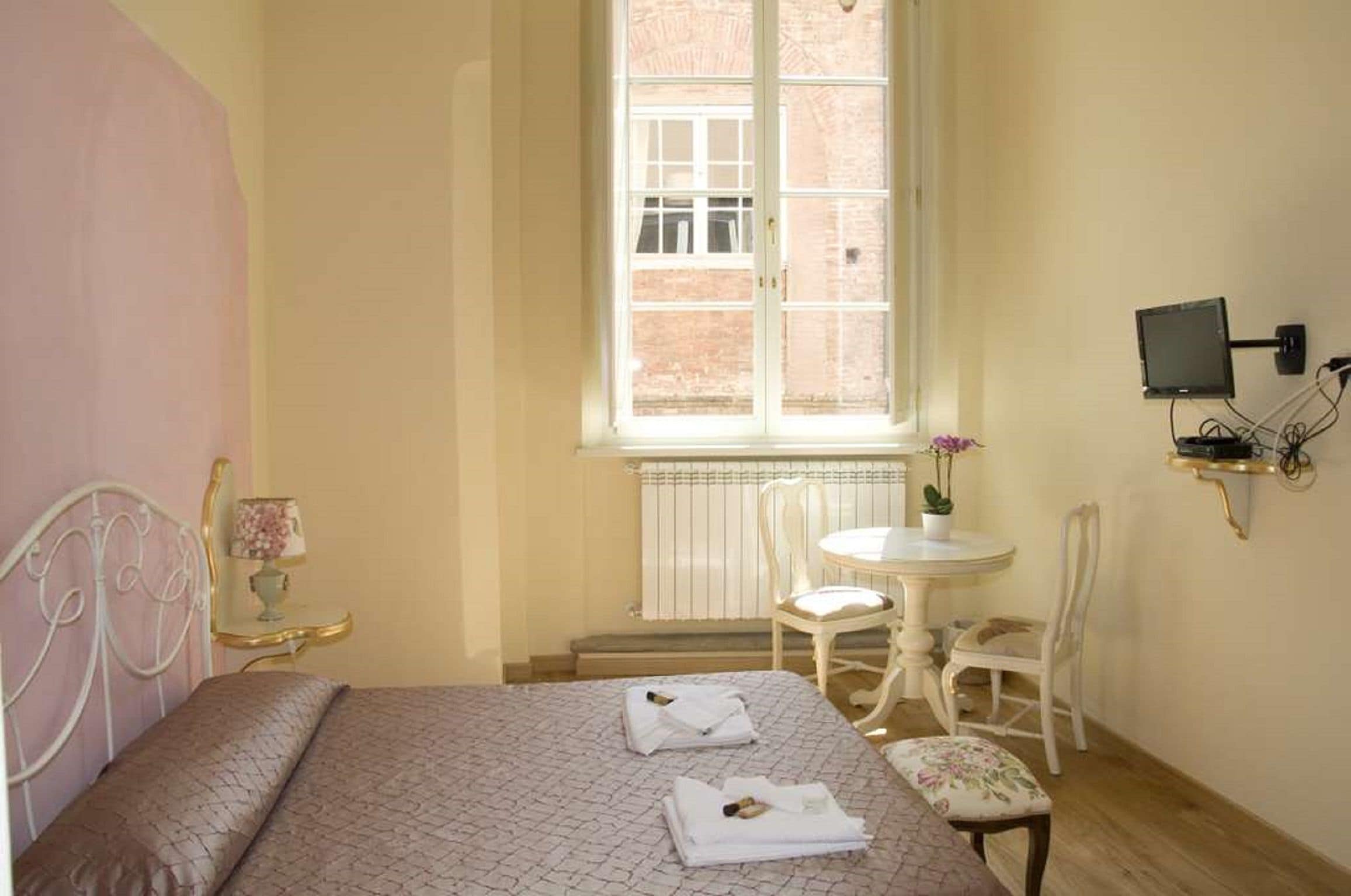 A bedroom with a bed, a window, a small table, a chair, and a TV mounted on the wall.