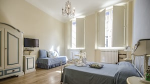 A bedroom with a large bed, a desk, a chair, a television, and a chandelier. - Anfiteatro Bed and Breakfast (Lucca)