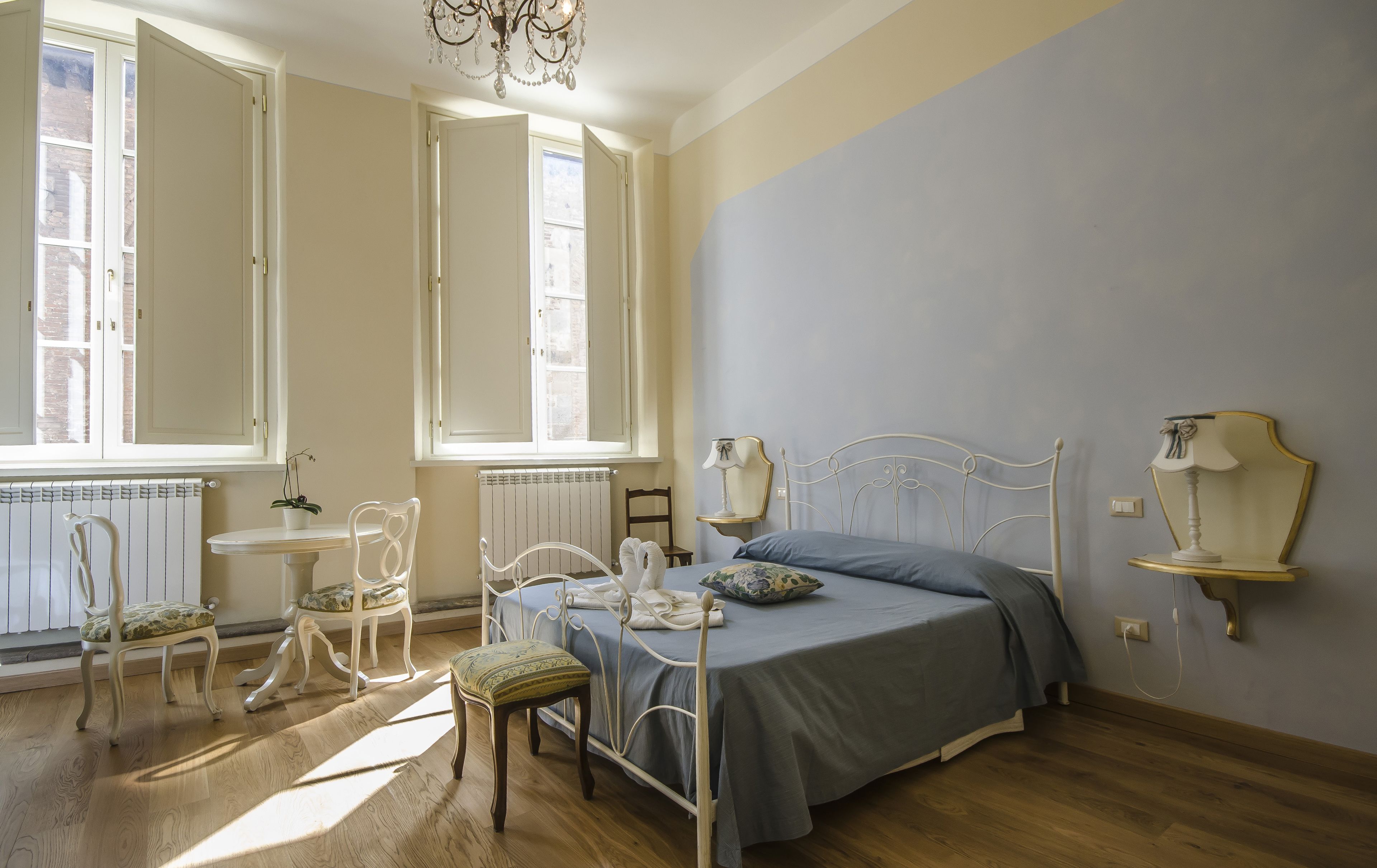 Un dormitorio con una cama, dos sillones, una mesa y una araña.