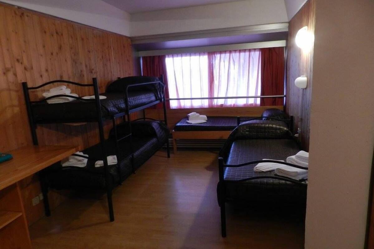 A dormitory room with bunk beds, a small table, and a window with curtains.