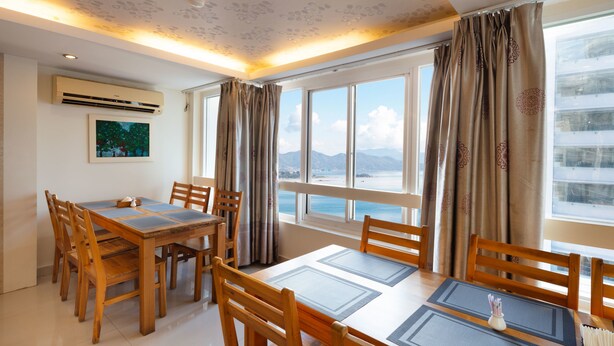 Ein Essbereich mit Tisch und Stühlen, großen Fenstern mit Vorhängen und Blick auf das Meer.
