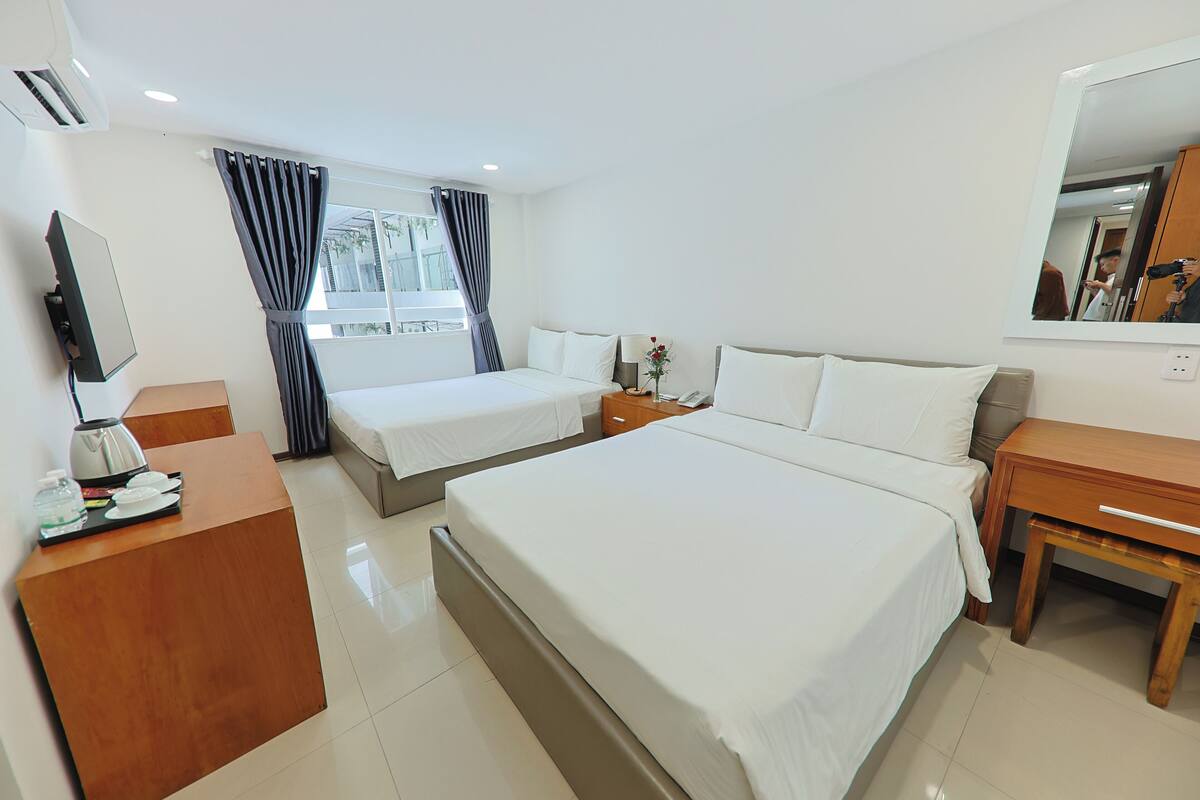 Quarto de hotel com duas camas, uma escrivaninha com telefone, um espelho e uma janela com cortinas.