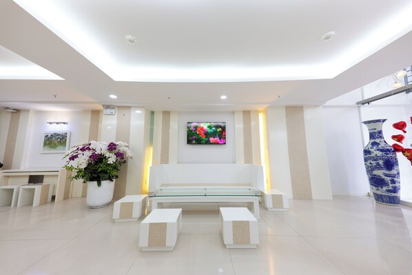 A modern reception area with a glass-top sofa, a potted plant, and a large vase. - Sea Light Hotel (Nha Trang)