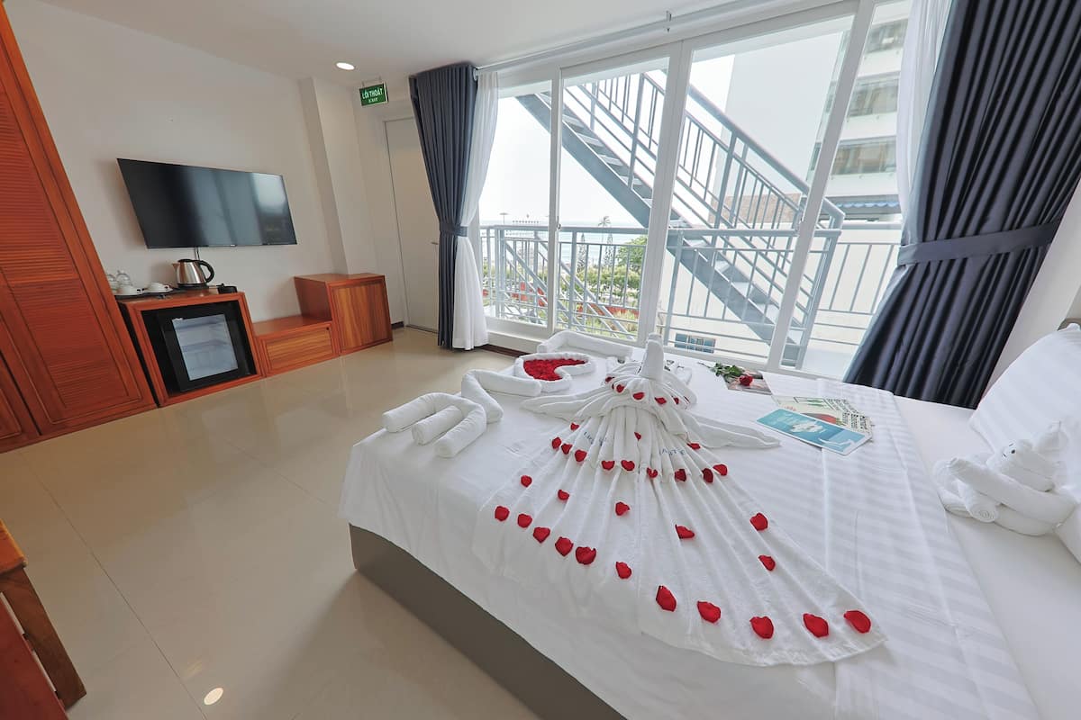 Quarto de hotel com uma cama grande, televisão de tela plana, cafeteira e vista para uma varanda com escadas.