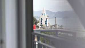Blick vom Balkon auf ein modernes Gebäude mit außergewöhnlicher Architektur, ein Gewässer und ferne Berge.