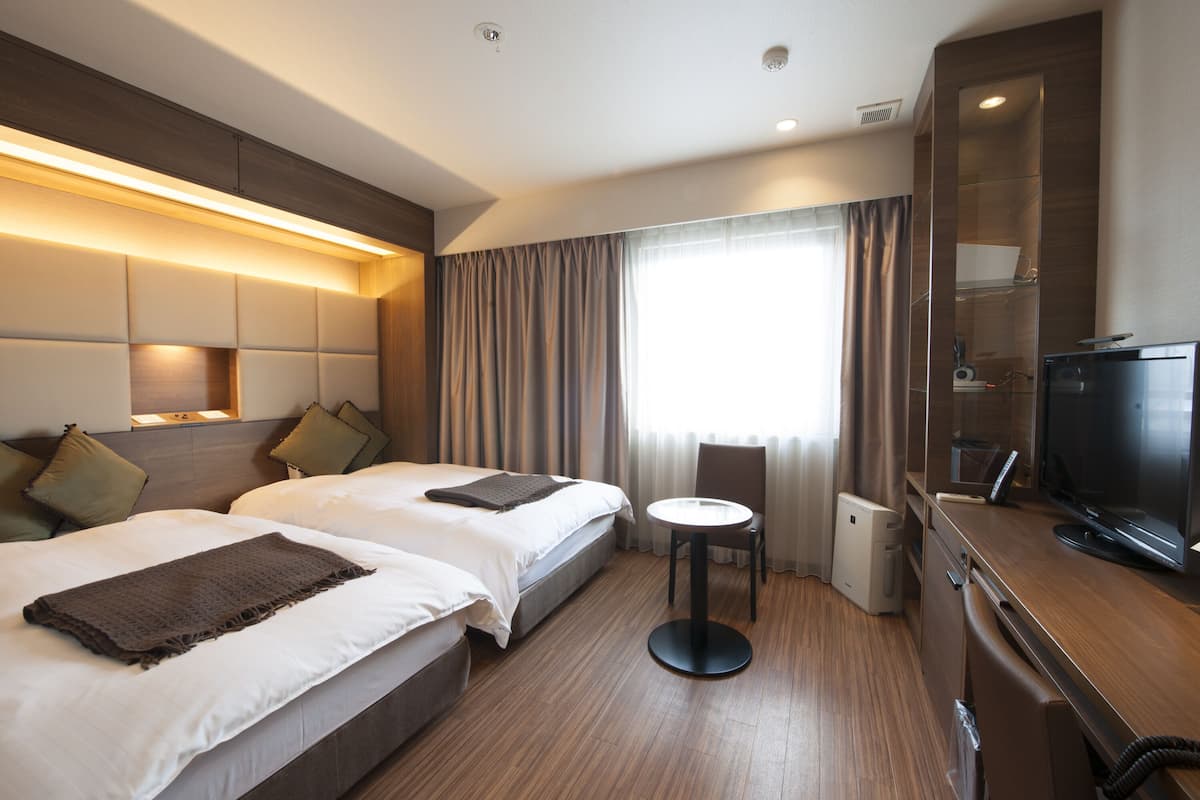 A hotel room with two beds, a small table, a TV, and a minibar.