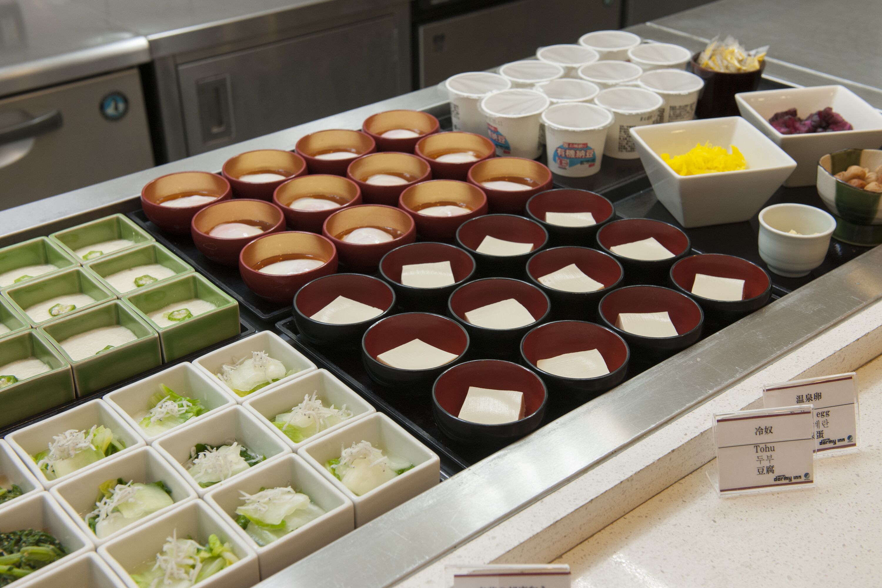Diversos recipientes e tigelas com comida sobre um balcão, possivelmente em um restaurante ou área de serviços de alimentação.