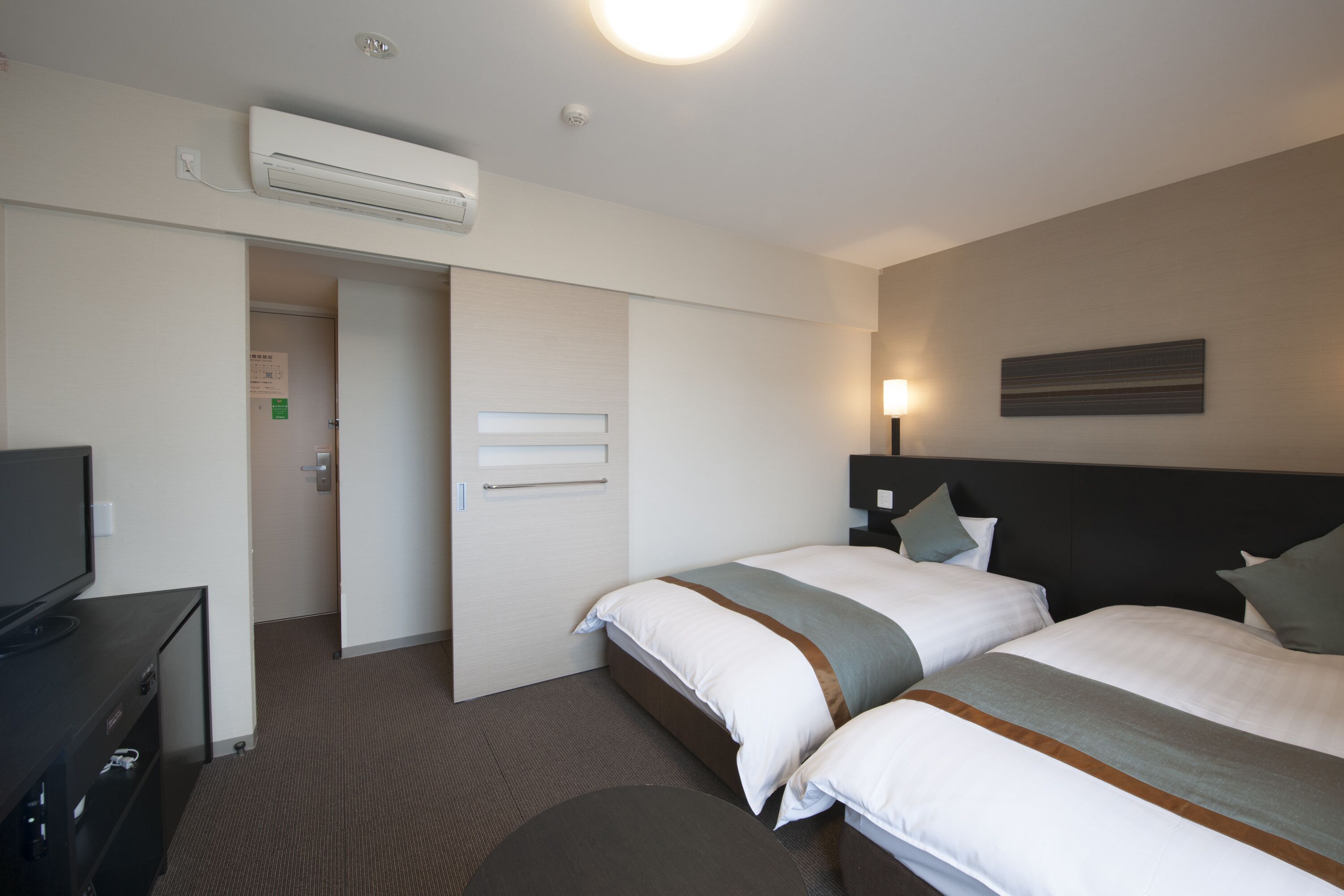 Una habitación de hotel con dos camas, televisor, escritorio y aire acondicionado.