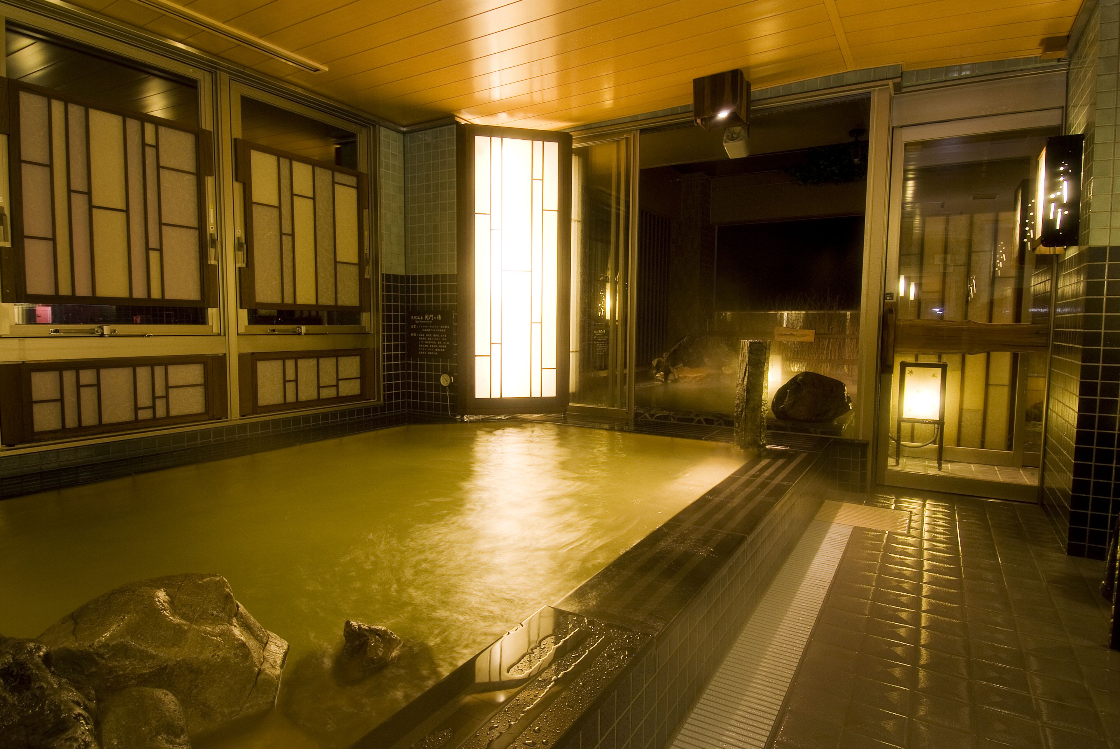 Un onsen japonés tradicional con interior de madera, tinaja de piedra y suelo de baldosas.