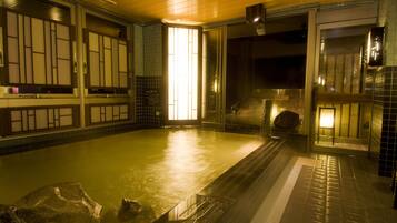 Un onsen japonés tradicional con interior de madera, tinaja de piedra y suelo de baldosas.