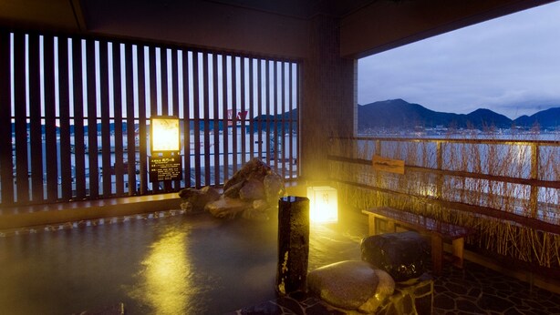A hot spring area with stone flooring, wooden benches, and a view of mountains.