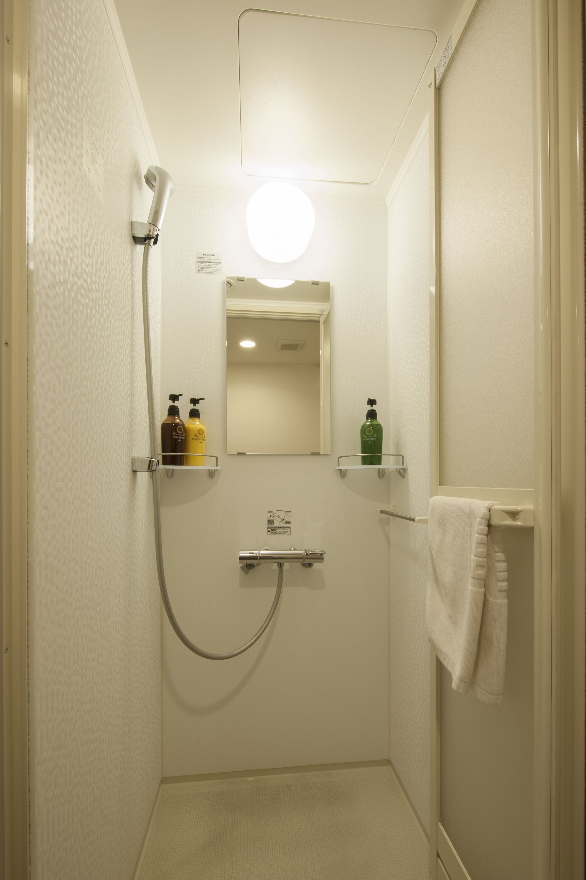 A small, enclosed shower area with a handheld showerhead, a mirror, and two shelves with toiletries.