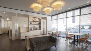 A modern hotel lobby with a sofa, dining area, and large windows.