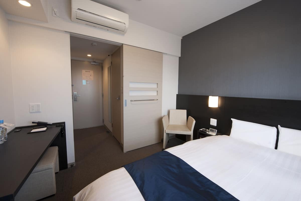 A hotel room with a bed, desk, chair, and a door leading to another room.