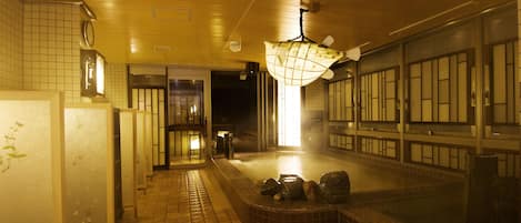 Un baño tradicional japonés con suelo de baldosas, una pila de piedra y una lámpara colgante.