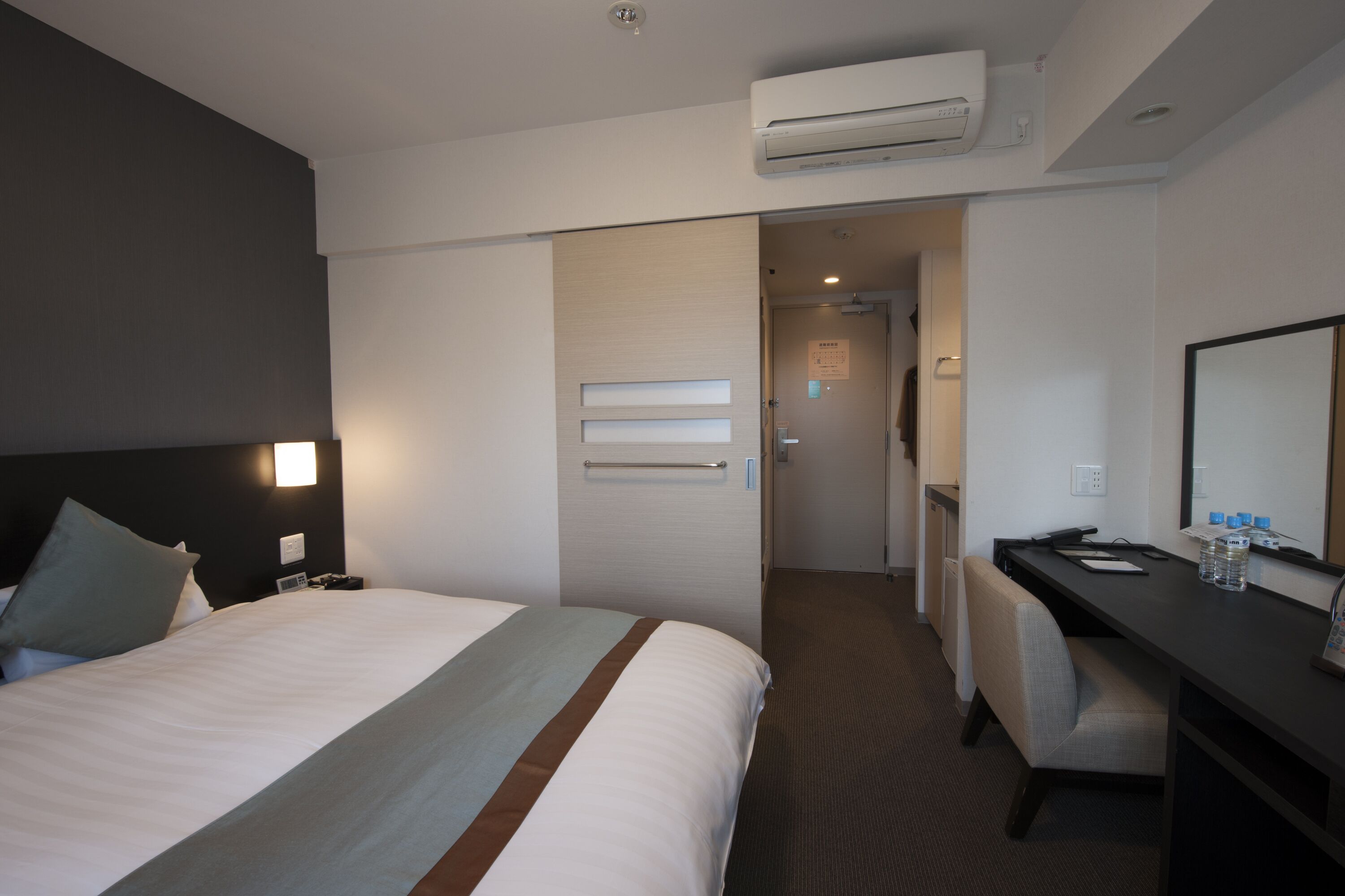 Een hotelkamer met een bed, nachtkastje, bureau, stoel en een airconditioning.