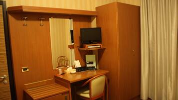 Une chambre d’hôtel de taille modeste, équipée d’un bureau en bois, d’une télévision, d’un ordinateur et d’une chaise.