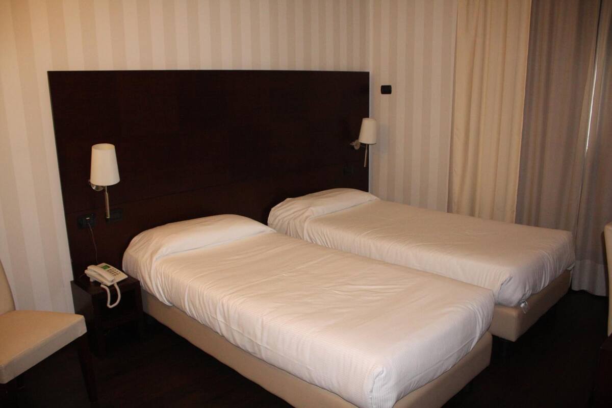 A hotel room with two single beds, a bedside table with a phone, and a chair.