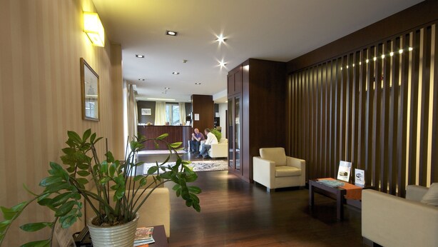 Un vestíbulo de hotel con mostrador de recepción, zona de estar y una planta grande en maceta.