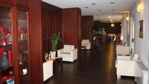 Un vestíbulo de hotel con paneles de madera, sofás blancos y una zona de recepción al fondo.