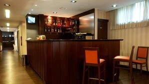 Una zona de bar con mostrador de madera, dos taburetes y un televisor fijado a la pared.