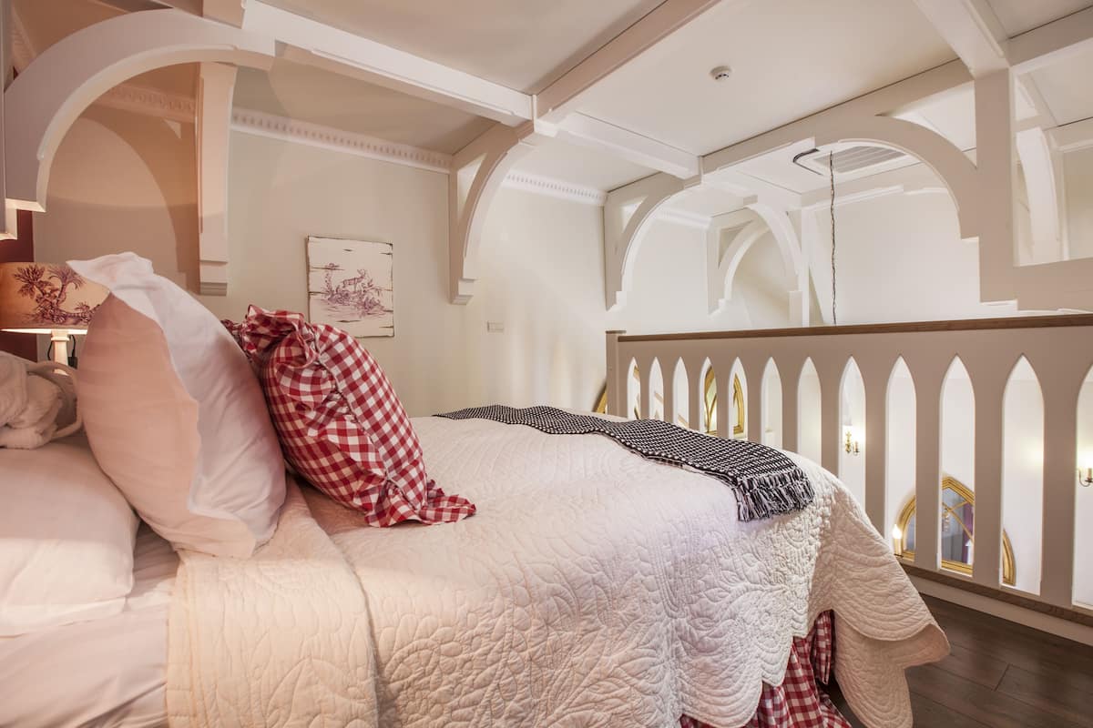 Quarto com cama grande, paredes brancas e tetos em arco.