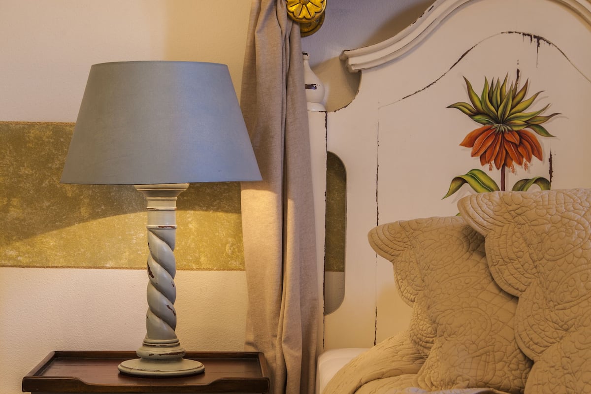Quarto com uma cama, mesa de cabeceira com abajur, cômoda e parede com decoração em trevo.