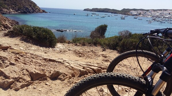 A rocky coastal path with a bicycle in the foreground and boats in the background. - Naranjos Resort Menorca (Sant Lluis)