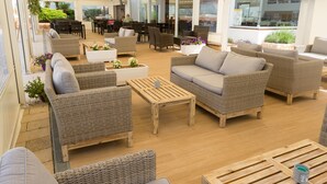 Un amplio espacio lounge al aire libre con mobiliario de mimbre, mesas de madera y plantas en macetas.