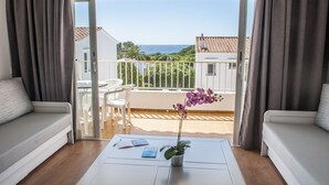 Un balcón con vistas al mar, un sofá blanco, una mesita con una planta y una silla.