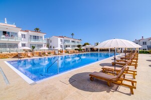 Una piscina al aire libre, sombrillas, sillones reclinables de piscina