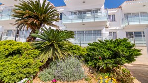 Un edificio moderno de varios pisos con balcones, rodeado de exuberante vegetación y diversas plantas.