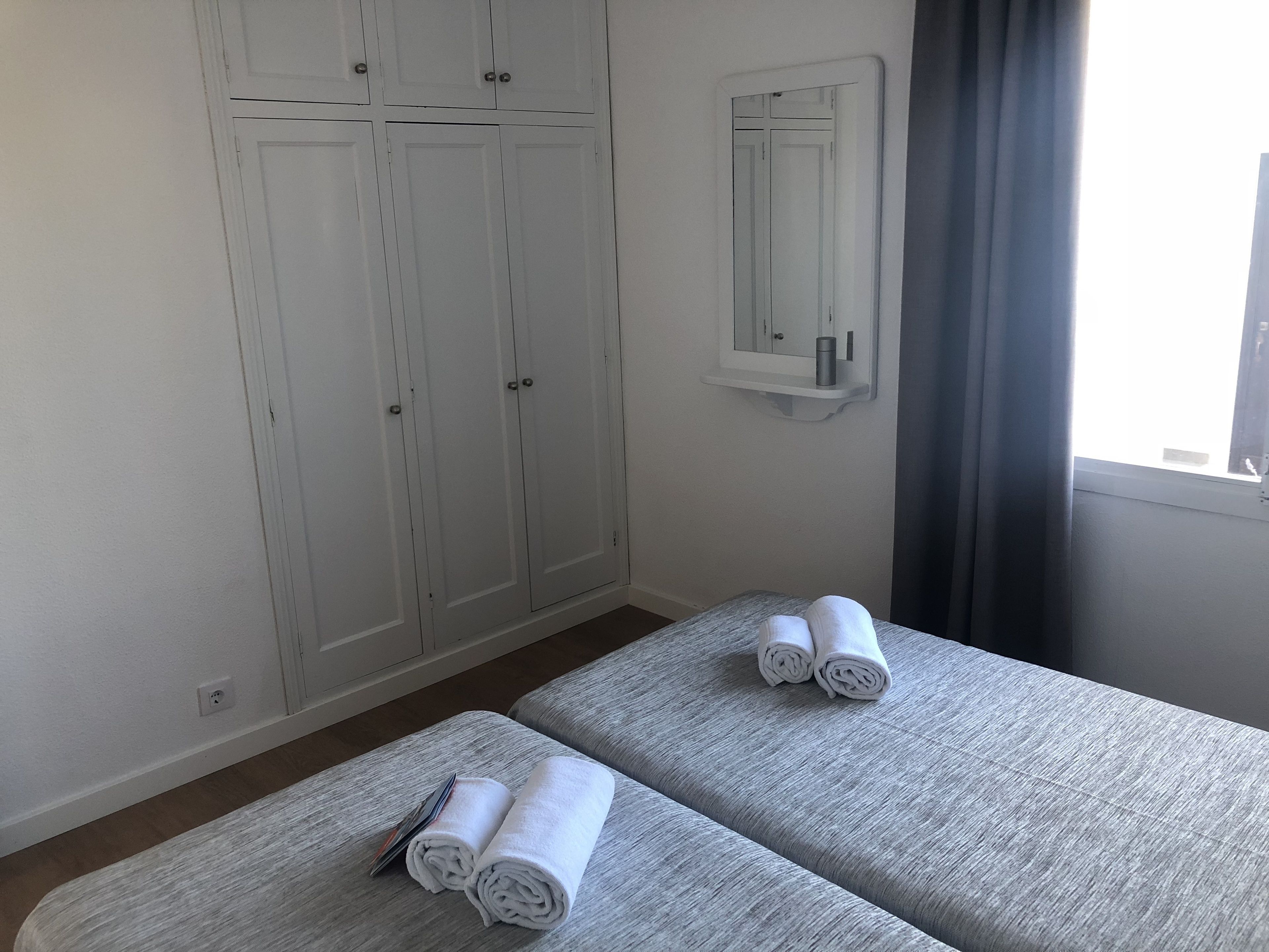 A room with two beds, a wardrobe, a mirror, and a window with curtains.