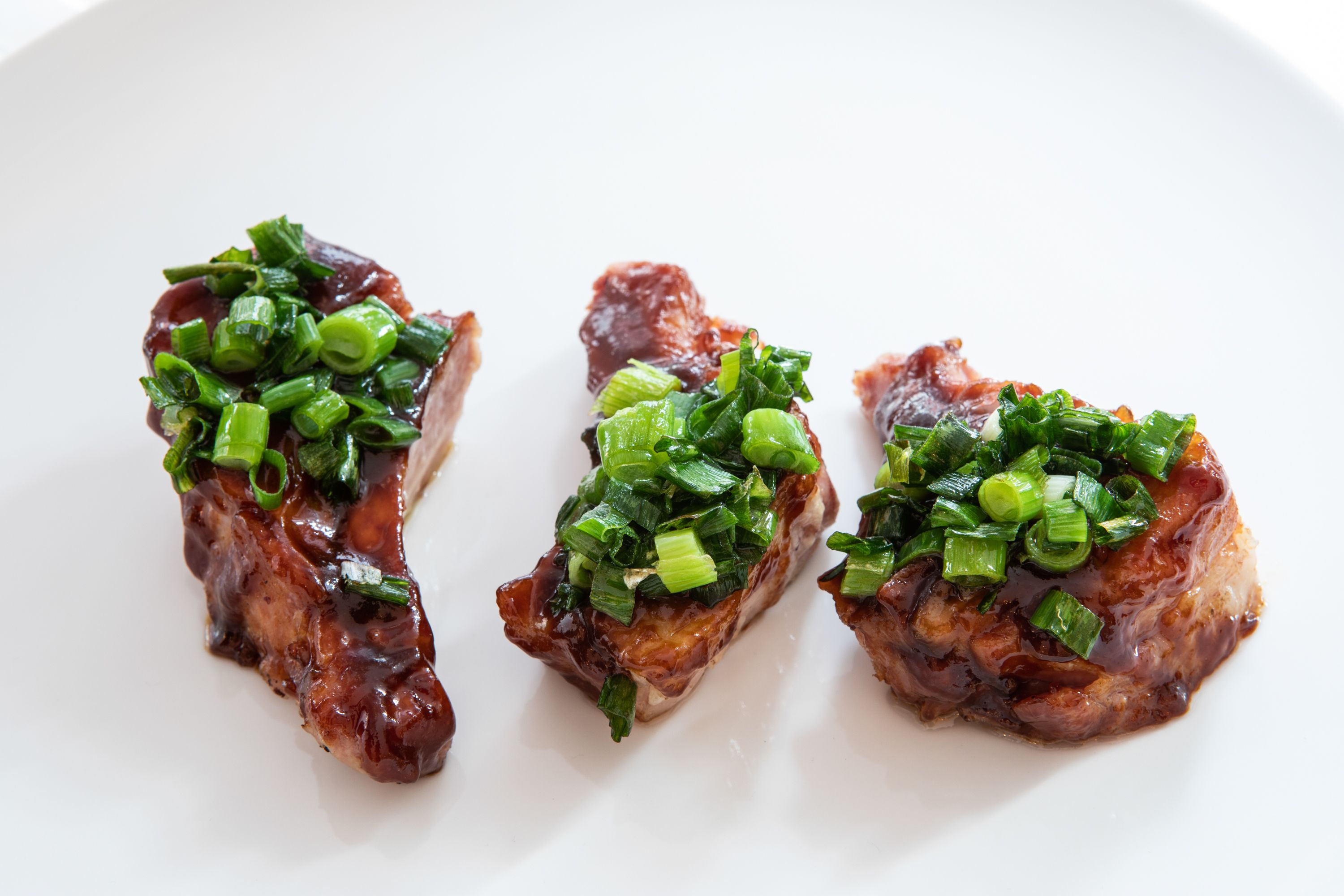 Trois morceaux de viande garnis d’oignons verts hachés, présentés sur une assiette blanche.