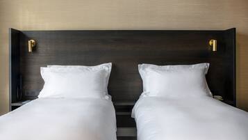 Un lit double avec du linge de lit blanc, une tête de lit en bois foncé et un téléphone sur la table de chevet.