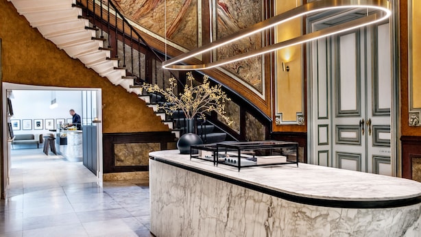 A lobby with a marble reception desk, a staircase with a marble wall, and a fireplace.