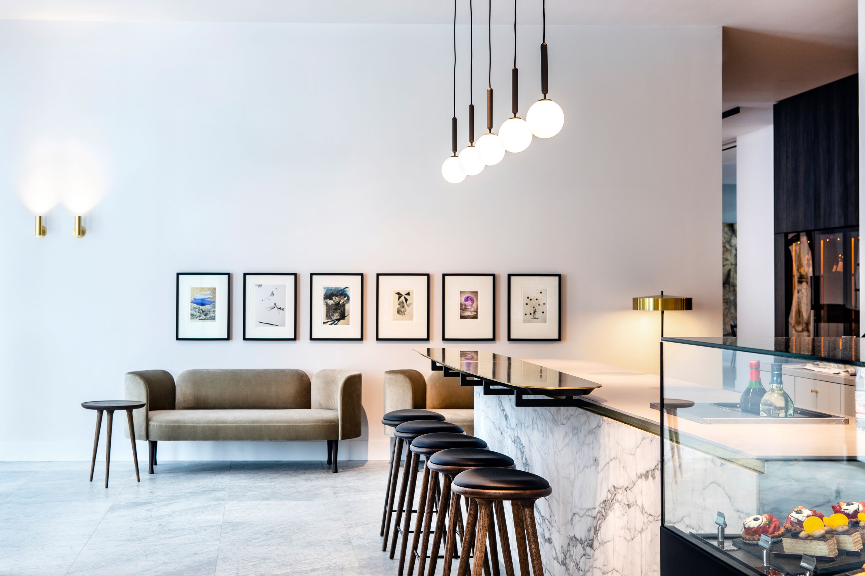 Zona de bar moderna con encimera de mármol, taburetes y cuadros en la pared.
