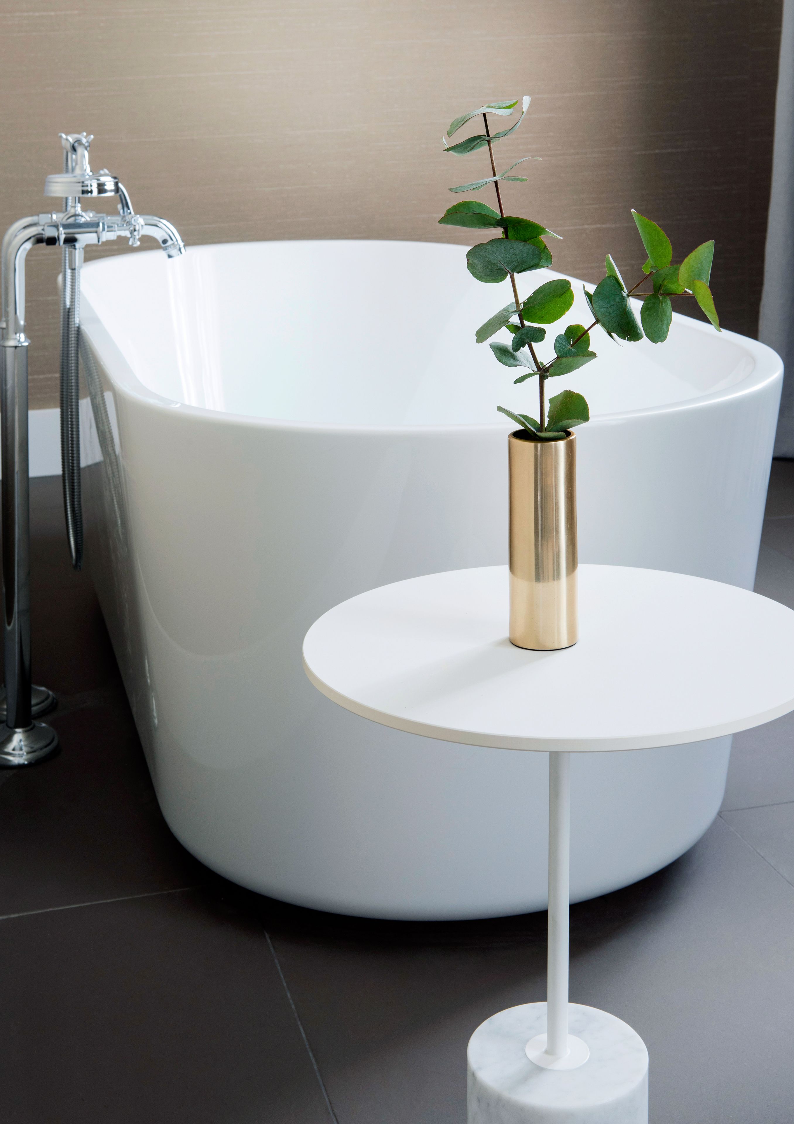 Een moderne badkamer met een vrijstaand bad, een klein rond tafeltje met een vaas, en een douchegedeelte.