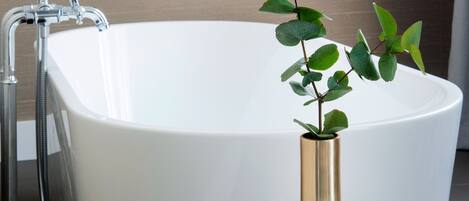 A modern bathroom with a freestanding bathtub, a small round table with a vase, and a shower area.