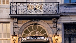 The exterior of the Grand Hotel with a classic arched entrance, ornate ironwork, and two wall-mounted lamps.