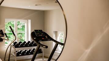 Un gimnasio en casa con cinta de correr, mancuernas y ventana con vista a follaje.