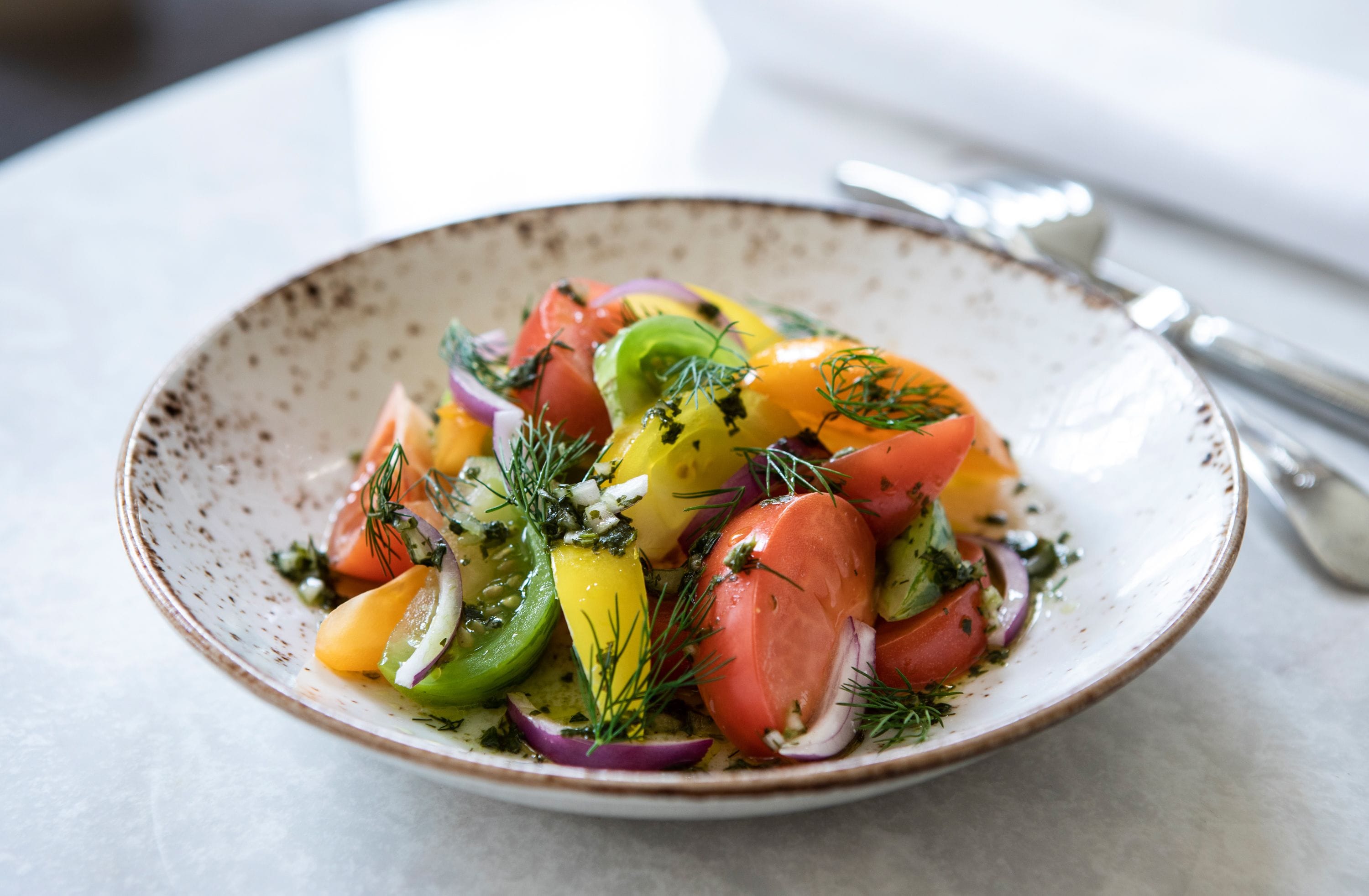 A bowl of colorful salad with various vegetables and herbs.